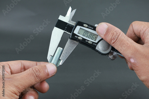 Hand measure diameter hex bolt using digital vernier caliper on black background. Universal tool for high-precision measurements of external and internal dimensions. Measurement tool.