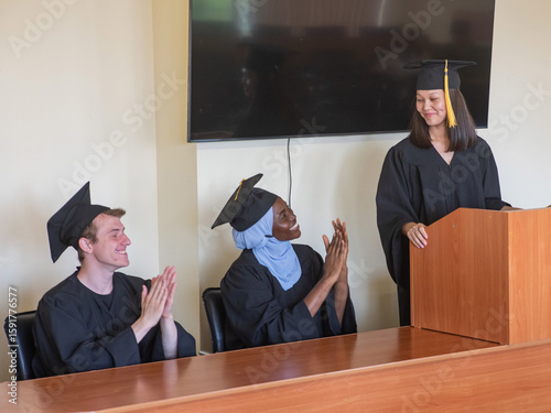 A young woman stands at the lectern and delivers a graduation speech to her classmates. 