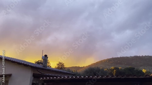 Dark orange cloud moving along the sky after strong thunderstorm, countryside houses and mountains in rainy weather, horror scene of nature after hurricane