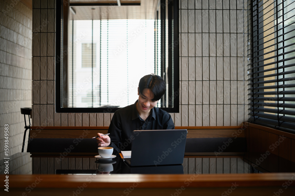 Fototapeta premium Casual professional workspace featuring a man smiling at his laptop with a cup of coffee