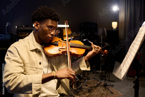 Quadro su tela Young adult Black man playing violin in music studio, focusing on sheet music wh