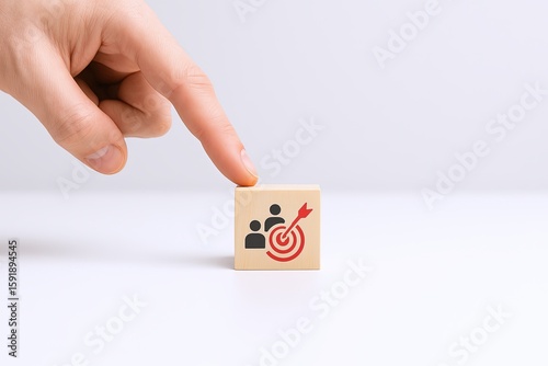 Hand pointing at small block with team and target icon for teamwork and strategy.