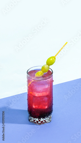 Honey Deuce cocktail with grapes on skewer and red-pink gradient lighting. Concept of iconic tennis drinks, creative cocktail styling, sweet vodka mixes, trending bar visuals.
