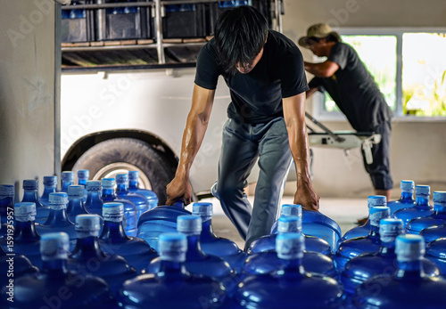 male warehouse worker lifting a Gallon drinking water, Workers transfer drinking water bottles from the production line to trucks in waterdrink factory