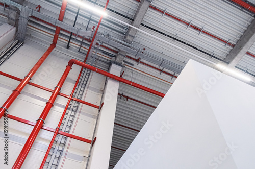 Interior view of an industrial ceiling with exposed red pipes and metal cable trays in a modern building.
