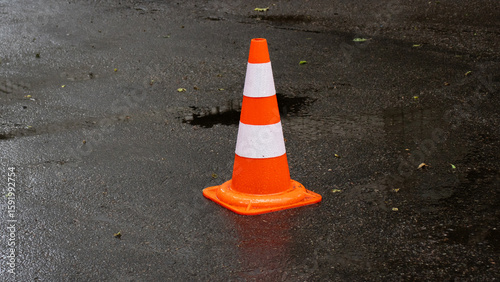 Traffic safety cone placed on a wet street after rainfall in an urban setting during morning hours