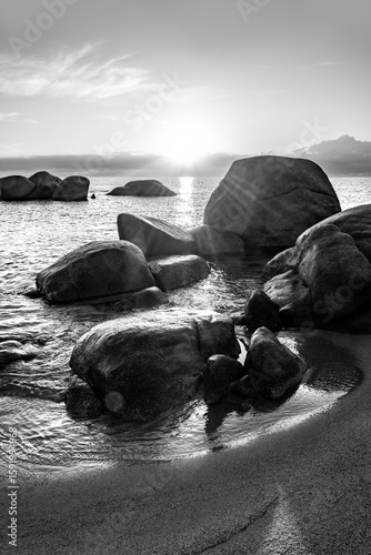 Fototapeta Naklejka Na Ścianę i Meble -  Rocks on the beach of Tortoli in the Mediterranean Sea in Sardinia (Italy) near Arbatax on the east coast of the popular vacation island. Black and white sunrise atmosphere on a summer morning.