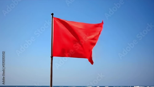 A bright red flag flutters in the wind against a clear blue sky