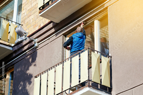 Man with trowel plastering external wall of residential building. Man on balcony applies putty on window jamb after window replacement. Installing new window, plastering works. Painting work