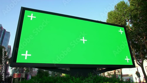 Green screen outdoor billboard with chroma key display and tracking marks in city street for advertising mockups.