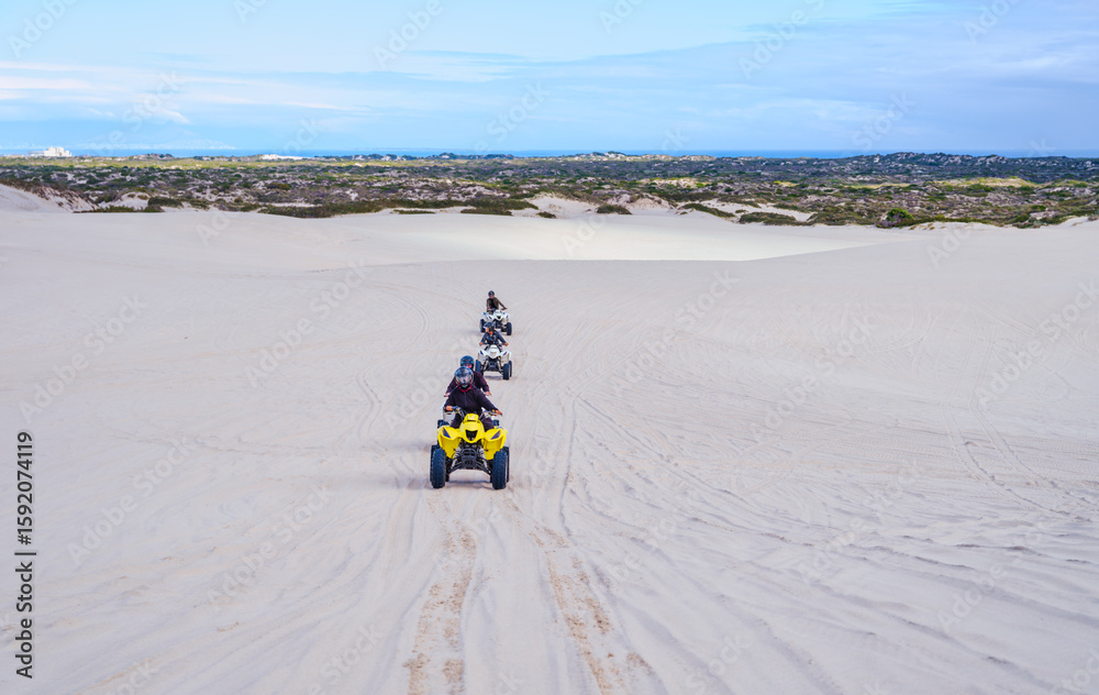 Fototapeta premium Four electric quad bikes driving in a line on white sand dunes, Atlantis, South Africa