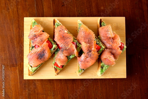 Tramezzini al salmone affumicato serviti su tagliere in legno, tagliati a triangolo. Eleganti e gustosi, perfetti per aperitivi o buffet. Fotografia realizzata con vista dall’alto.