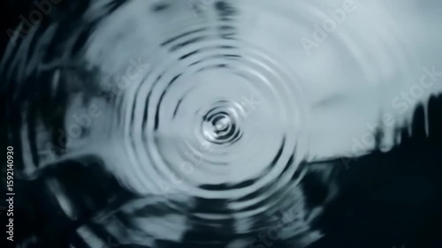 Dramatic top-down slow motion close-up of a water drop creating concentric ripples on a dark liquid surface
