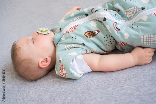 Baby boy in sleeping bag sleeping on parent's bed. Child is 6 months old.	