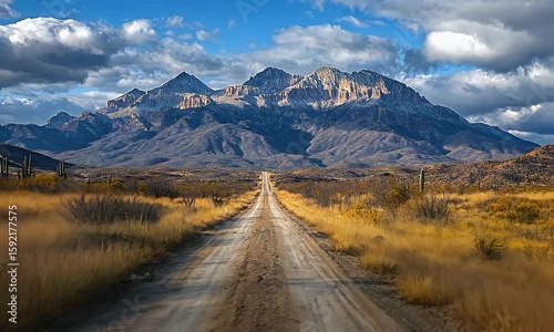 Serene dirt road leading through golden grasslands towards majestic mountains under a blue sky