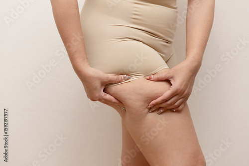 Wallpaper Mural Close-up of a woman in nude shapewear pinching fat on her upper thigh, highlighting cellulite or targeted fat area Torontodigital.ca