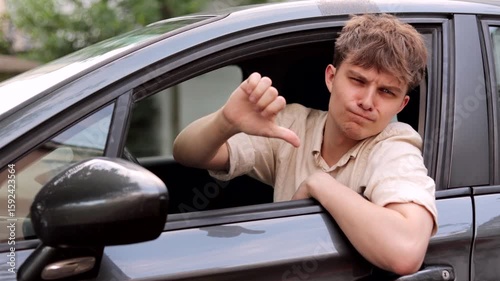 Sad young driver showing thumbs down in car. Bad customer service by repair shop