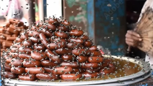 Flies swarm over uncovered sweets at a roadside stall in India, raising concerns about hygiene and food safety in open-air street food environments.