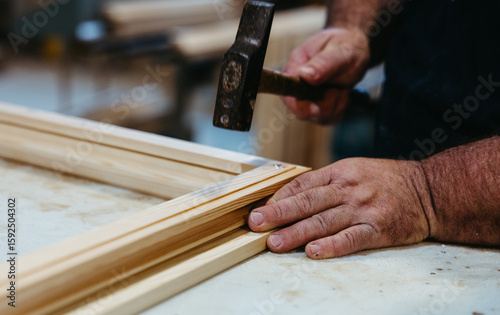 Close-up of carpenter hammering wooden window frame in workshop