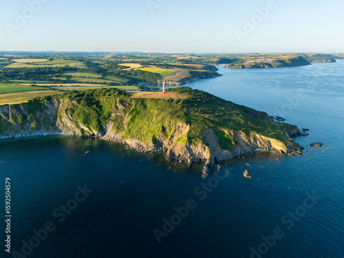 Aerial view of the emerald headland embraced by the deep blue sea, with a lighthouse standing sentinel against the horizon, Fowey, England, United Kingdom.