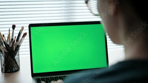 Woman working on a laptop with green screen for easy keying and graphics insertion, ideal for remote work and digital projects.