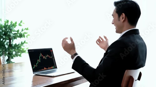 Asian professional analyses stock market data and charts on laptop, wearing suit