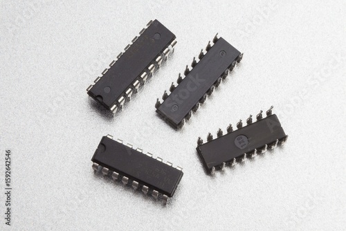 Black plastic electronic microchips with metallic pins are arranged on a reflective surface