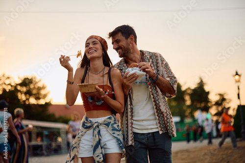 Happy couple of festival goers eating after open air music concert in summer.