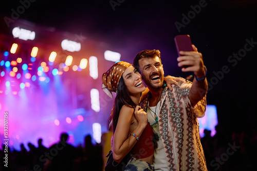 Happy festival goers taking selfie on summer music concert at night.