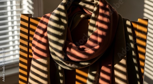 A cozy scarf draped over a wooden chair bathed in sunlight creating striped shadows with warm and cool tones.