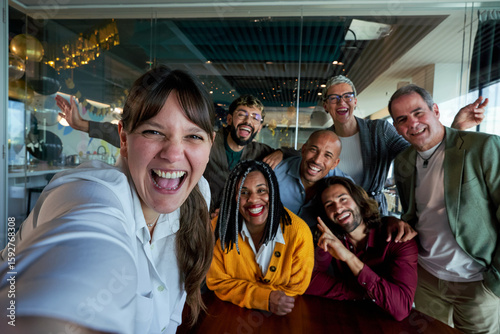 Valokuva Caucasian woman next to diverse businesspeople smiling and taking a selfie together in a bright, modern office, showing on social media teamwork and camaraderie between work