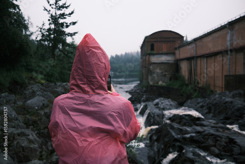 A girl in a pink raincoat taking a photo of a mountain river