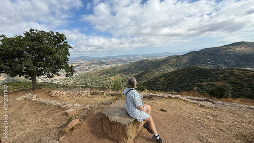 Photography Breathtaking View of the Barcelona Mountains with a Lone Figure Sitting on a Sto