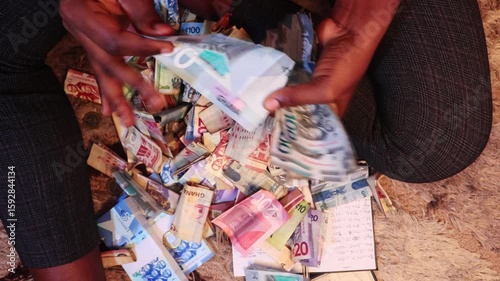 Black African person counting staightening unfolding arranging and counting Ghanaian cedi notes on woolly carpet floor. close up top view
