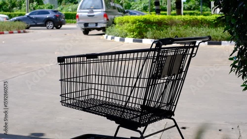 A shopping cart is sitting in a parking lot. The parking lot is empty except for a few cars