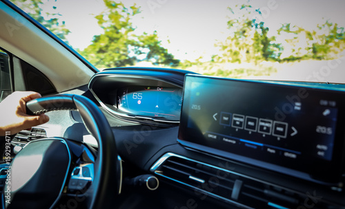 Modern digital dashboard view inside a moving car with a driver's hand on the wheel. Navigation system and infotainment screen showing active driving status