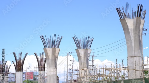 A group of tall concrete pillars are being built. The sky is clear and blue. The pillars are in various stages of construction