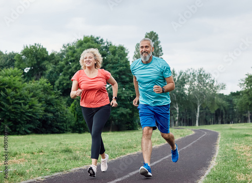 Smiling active mature middle aged couple jogging together in the park