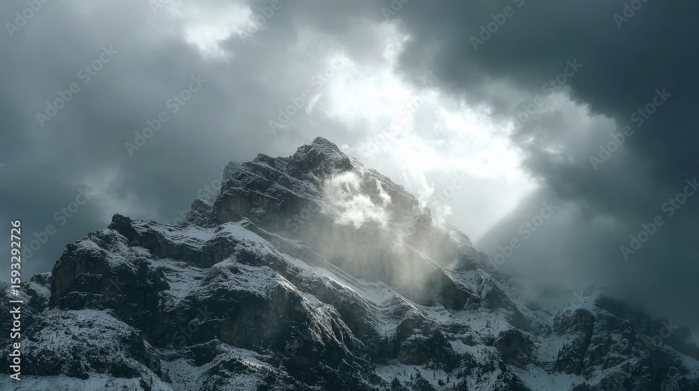 Fototapeta premium Rocky mountain summit under stormy clouds with sunlight breaking through