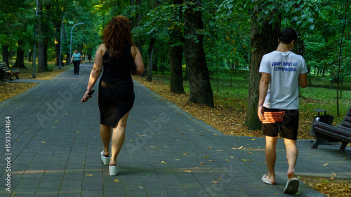 Fototapeta Naklejka Na Ścianę i Meble -  People walking on a tree-lined path in a park during a sunny day in summer