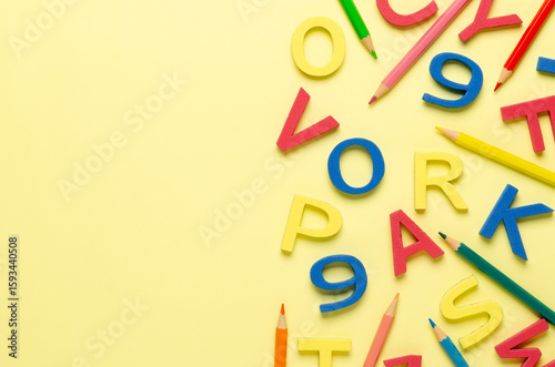 Colorful foam letters, numbers pencils on yellow background with copy space.