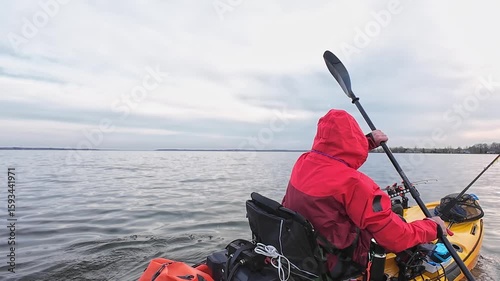 Fisherman sitting in kayak and paddling to the secret spot to catch fish. Kayak fishing competition action. Angler in dry suit or drysuit for environmental protection and cold water.