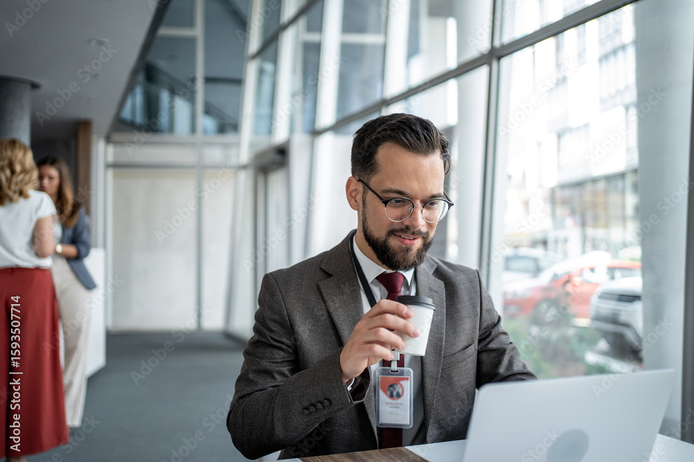 Businessman drinking coffee while working on laptop in office lobby Businessman drinking coffee while working on laptop in office lobby