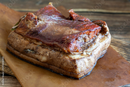 Pieces of smoked lard with layers of meat lie on paper on wooden background