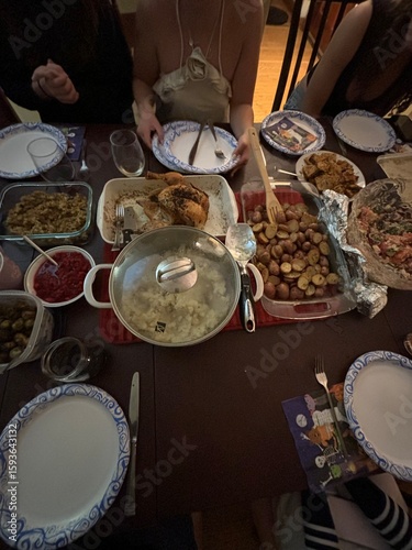 Family dinner table set with multiple dishes including roasted potatoes, meat, casseroles and blue patterned plates creating warm home-cooked meal gathering atmosphere