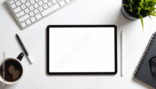 Top view of a tablet with a blank screen, surrounded by a keyboard, coffee, pen, plant, and notebook on a white surface.