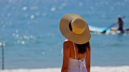 Woman in Hat Gazing at Ocean Paddleboarder: Serene Beach Scene