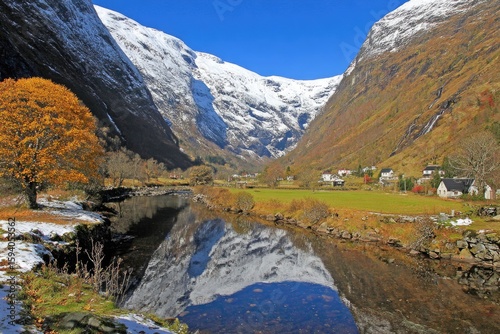 Autumnal mountain valley with snow-capped peaks reflected in a calm river