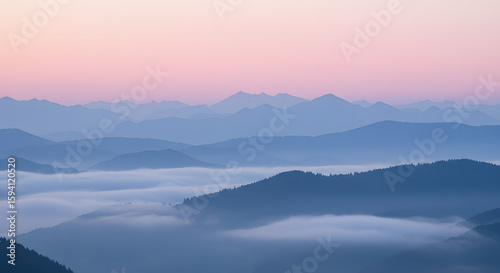 Misty mountain range landscape at dawn with layers of blue hills and a soft pink sky.