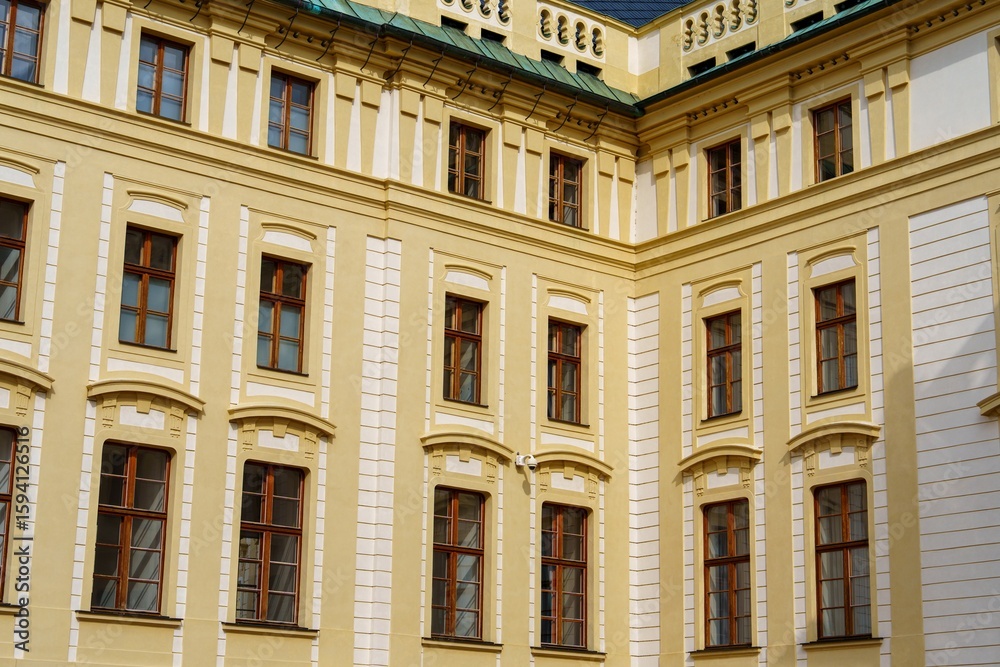 Obraz premium Discover the architectural beauty of a historic building in Prague. This facade features ornate windows and vibrant yellow walls, showcasing the city s rich design heritage.